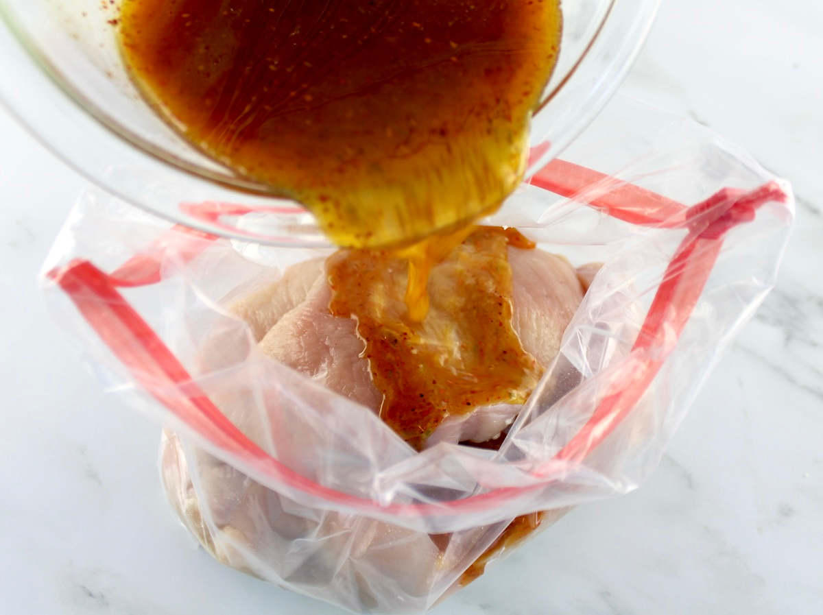 tajin lime marinade being poured over raw chicken in food storage bag