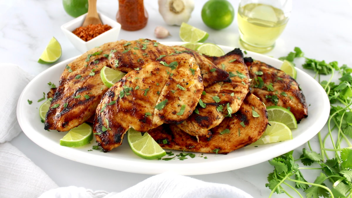 Grilled Tajin Chicken on white oval platter with chopped cilantro and lime slices