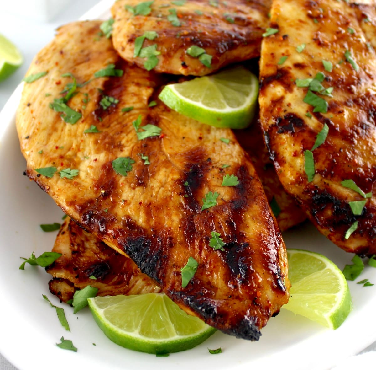 closeup of Grilled Tajin Chicken on white plate with chopped cilantro and lime slices