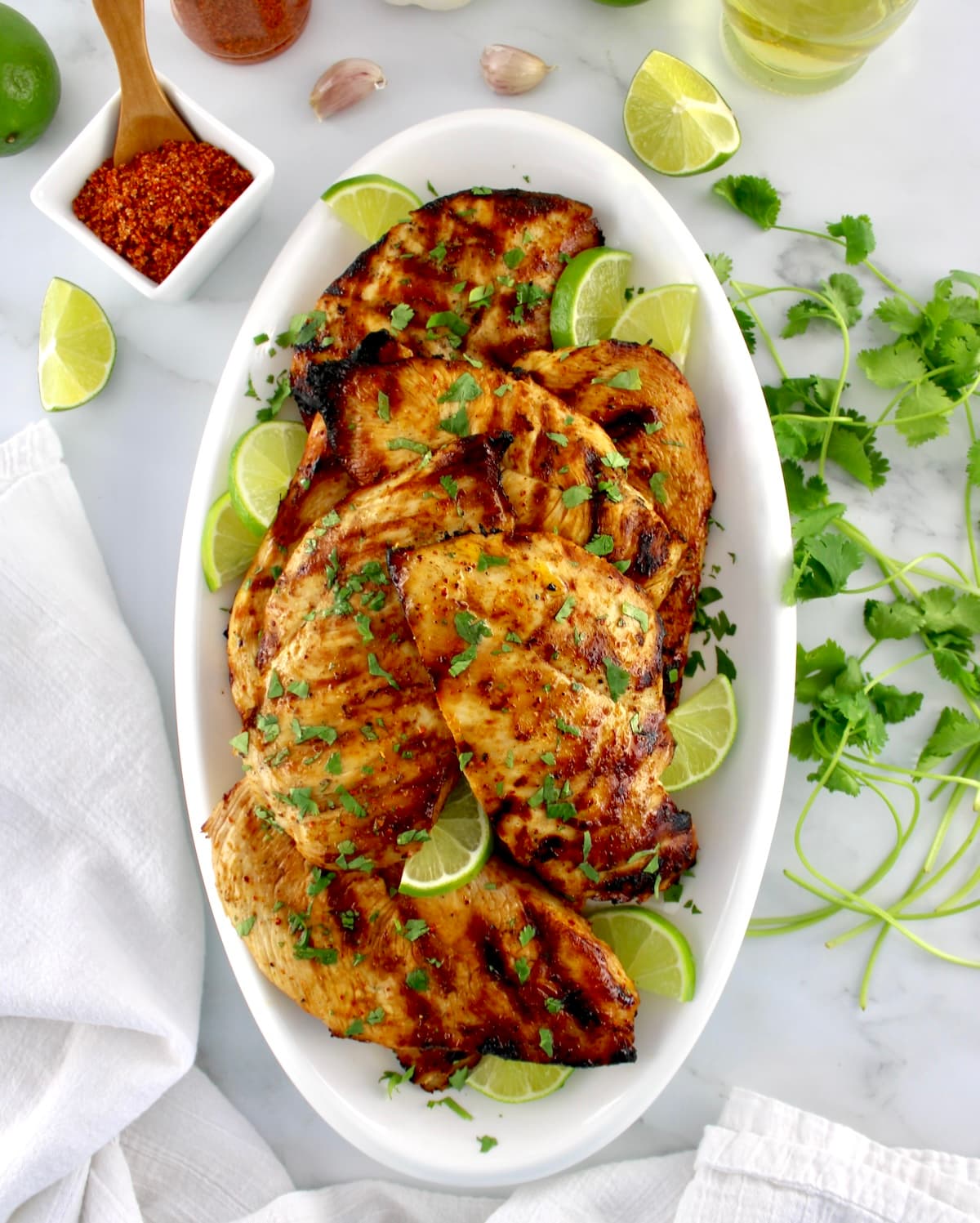 overhead view of Grilled Tajin Chicken on white oval platter with cilantro and lime slices