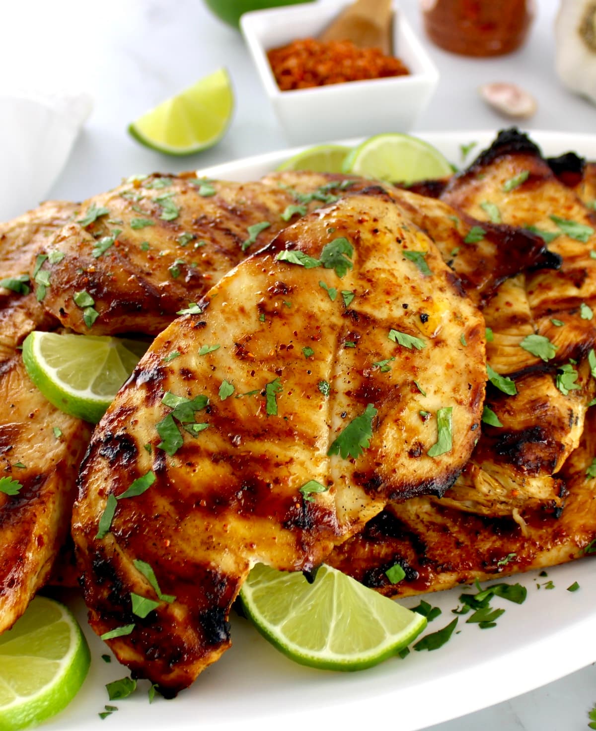 closeup of Grilled Tajin Chicken on white plate with chopped cilantro and lime slices