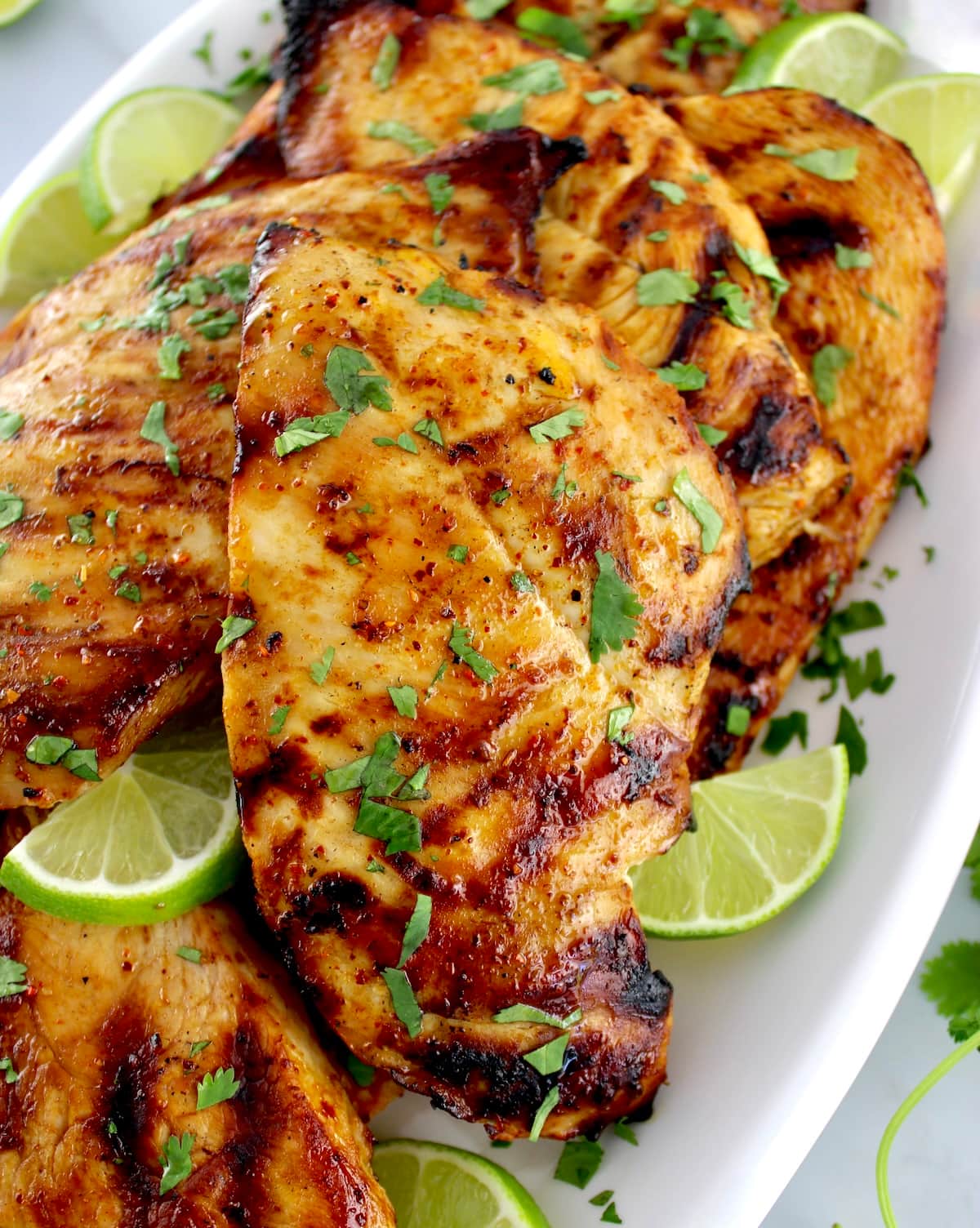 closeup of Grilled Tajin Chicken on white plate with chopped cilantro and lime slices