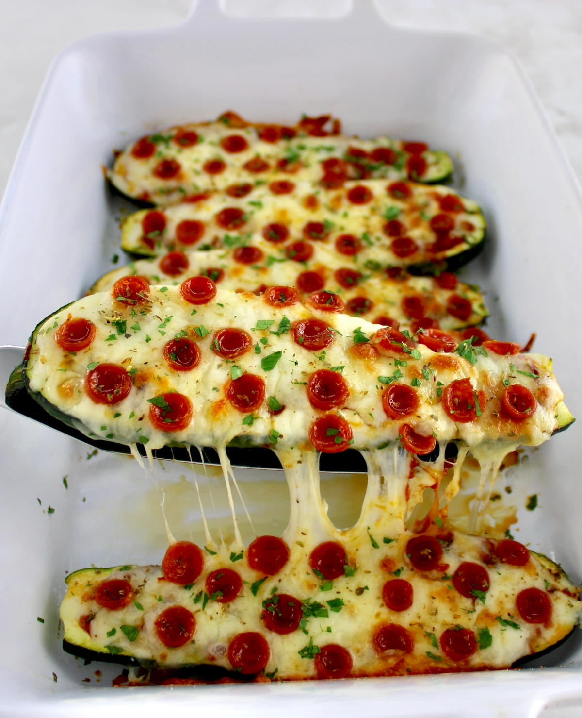 Zucchini Pizza Boat being lifted out of white casserole