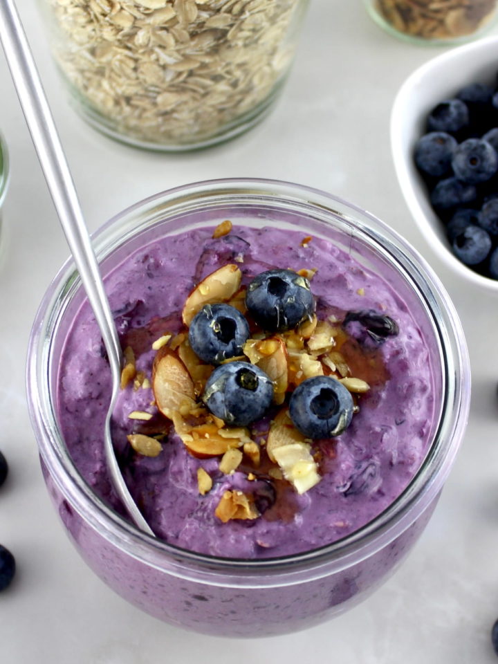 Blueberry Overnight Oats in glass jar with spoon and blueberries with almonds on top