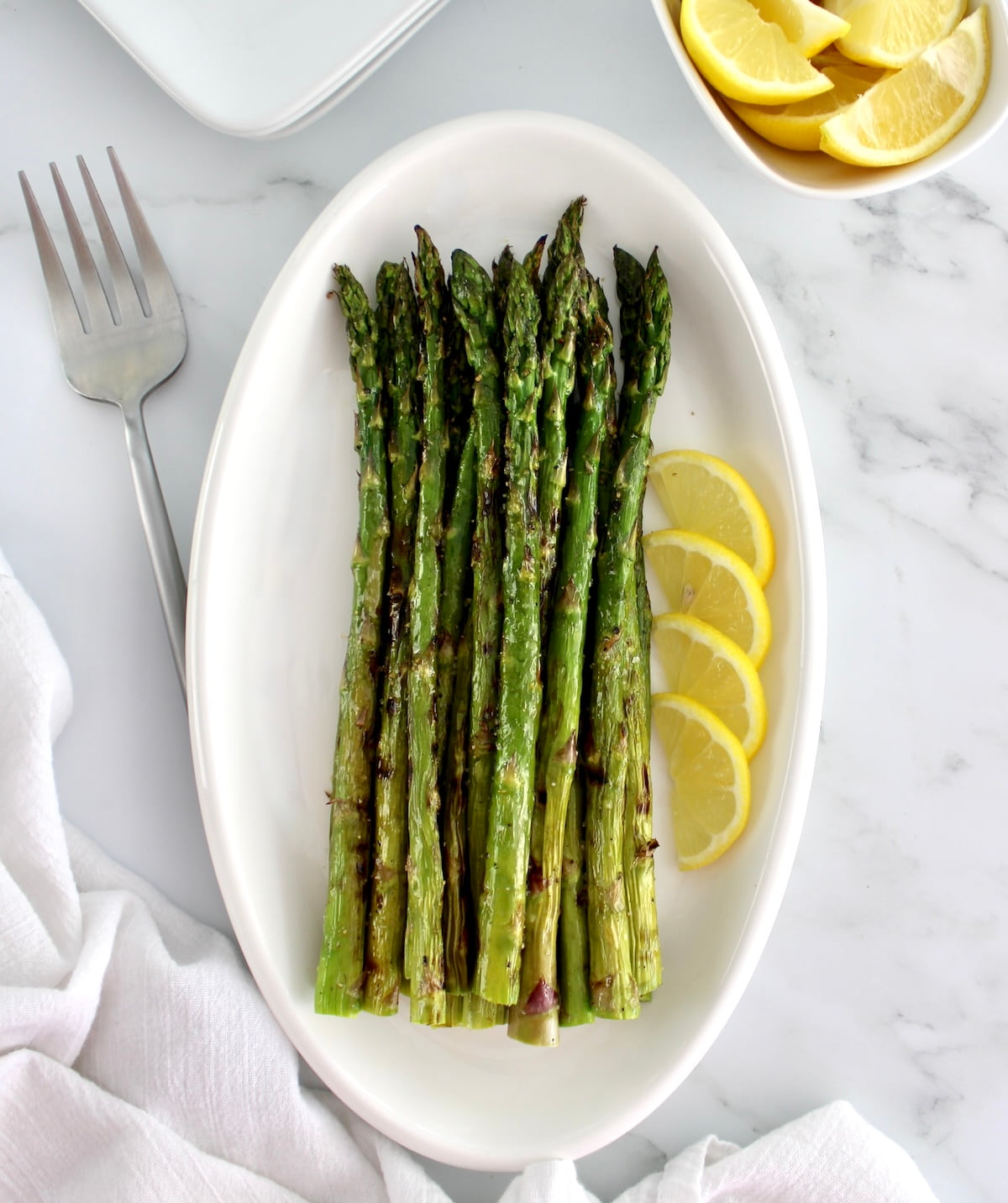 overhead view of Easy Grilled Asparagus on white oval platter with lemon slices