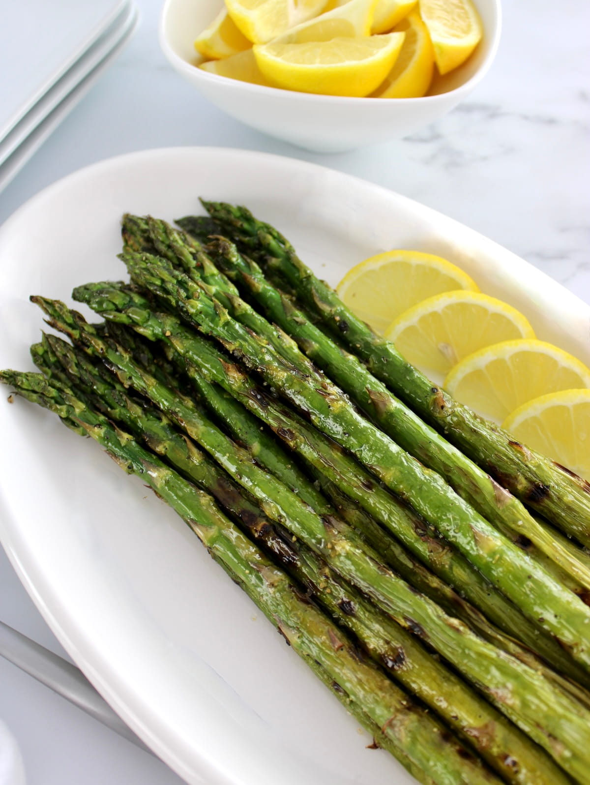closeup of Easy Grilled Asparagus on white plate with lemon slices