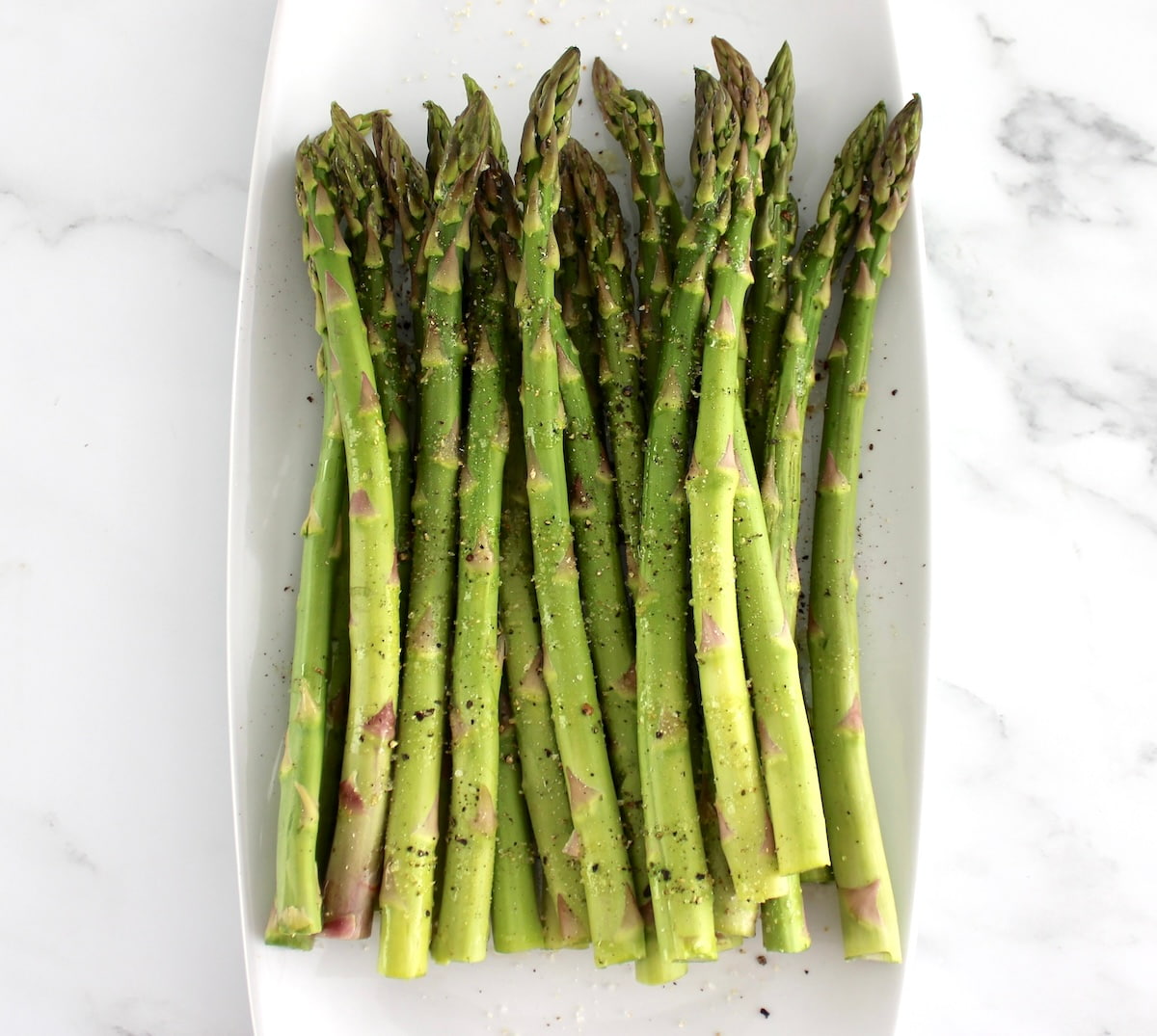raw asparagus on white plate with olive oil, salt and pepper