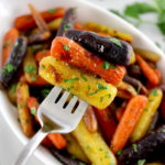 holding up 3 Honey Roasted Rainbow Carrots on fork over white bowl with more
