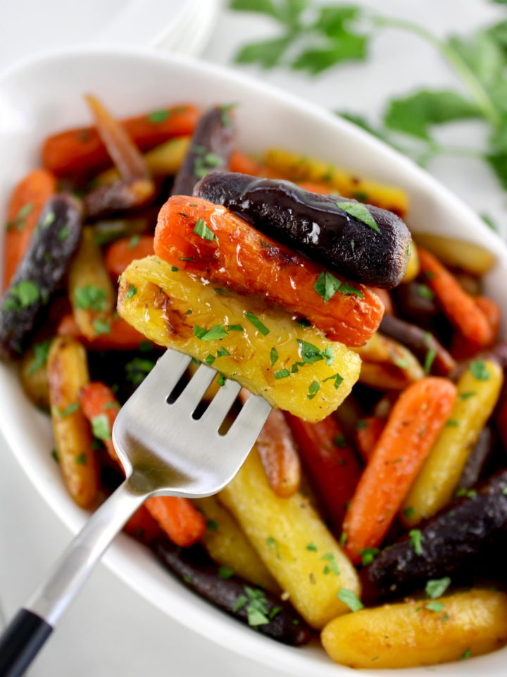 holding up 3 Honey Roasted Rainbow Carrots on fork over white bowl with more