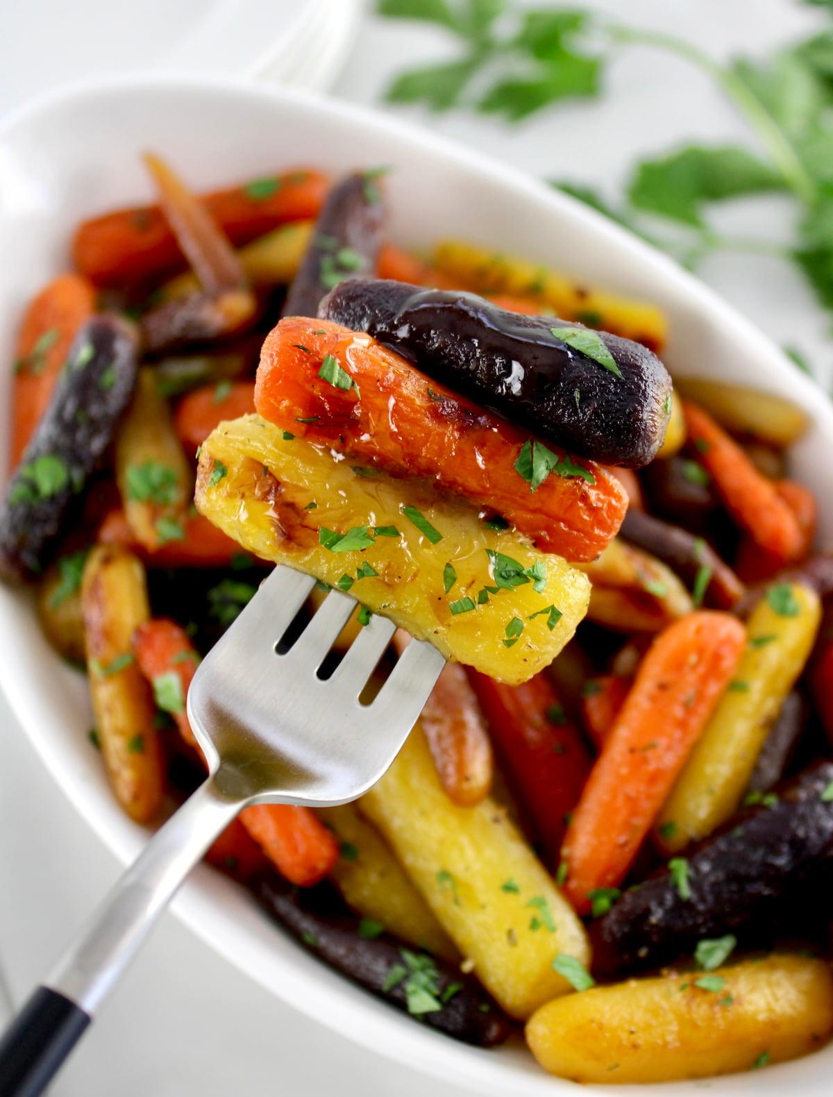 holding up 3 Honey Roasted Rainbow Carrots on fork over white bowl with more