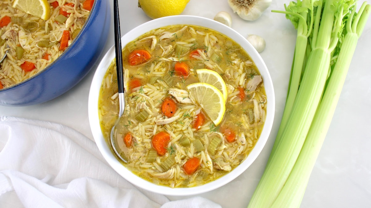 overhead view of Lemon Orzo Chicken Soup in white bowl with veggies in back