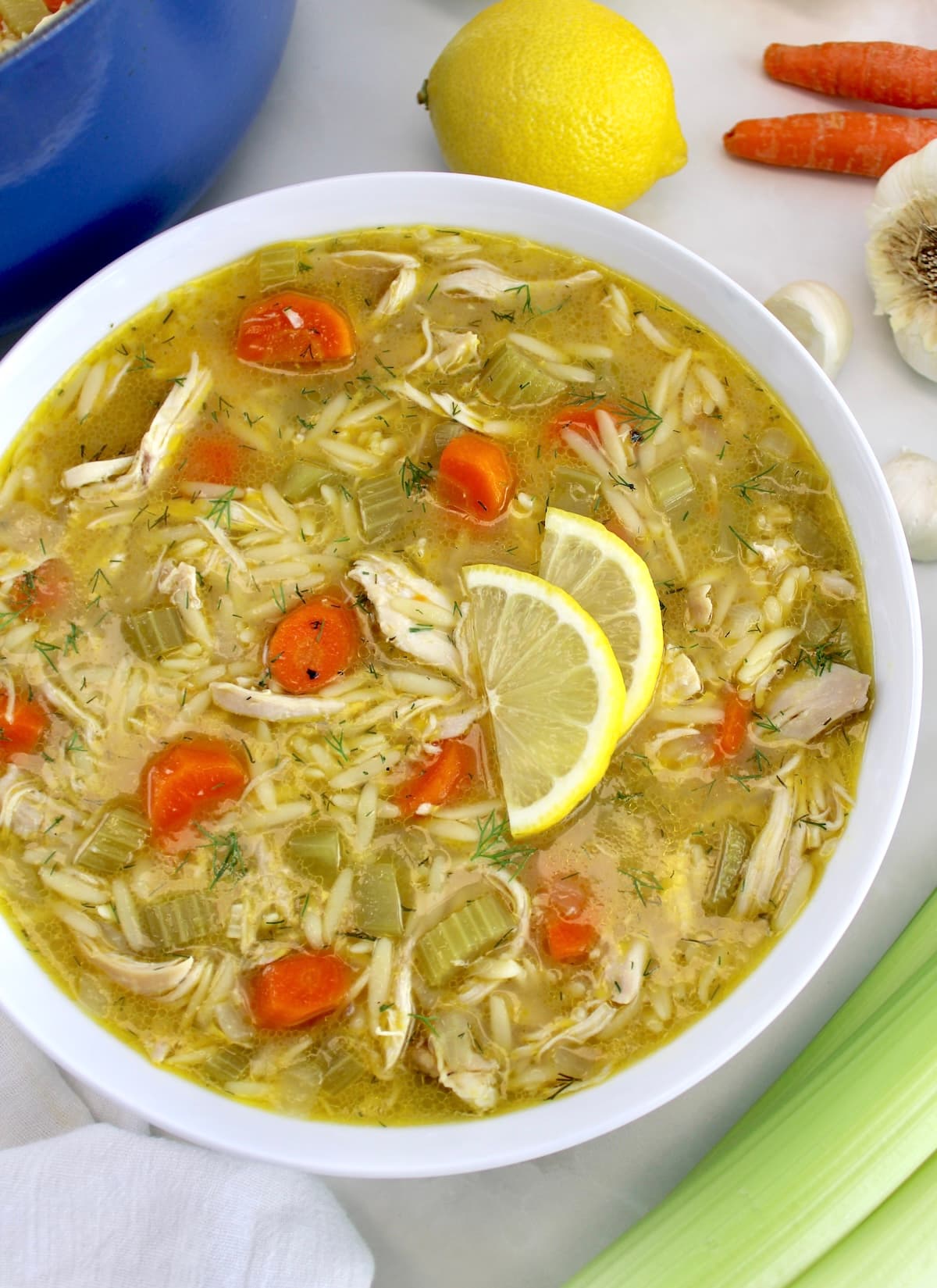 overhead view of Lemon Orzo Chicken Soup in white bowl with lemon slices