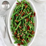overhead view of Green Beans with Crispy Prosciutto on white oval platter with serving utensils on side