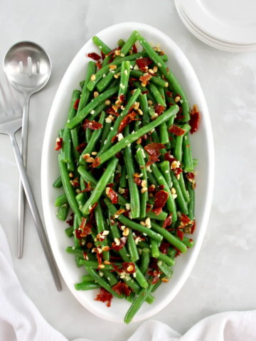 overhead view of Green Beans with Crispy Prosciutto on white oval platter with serving utensils on side