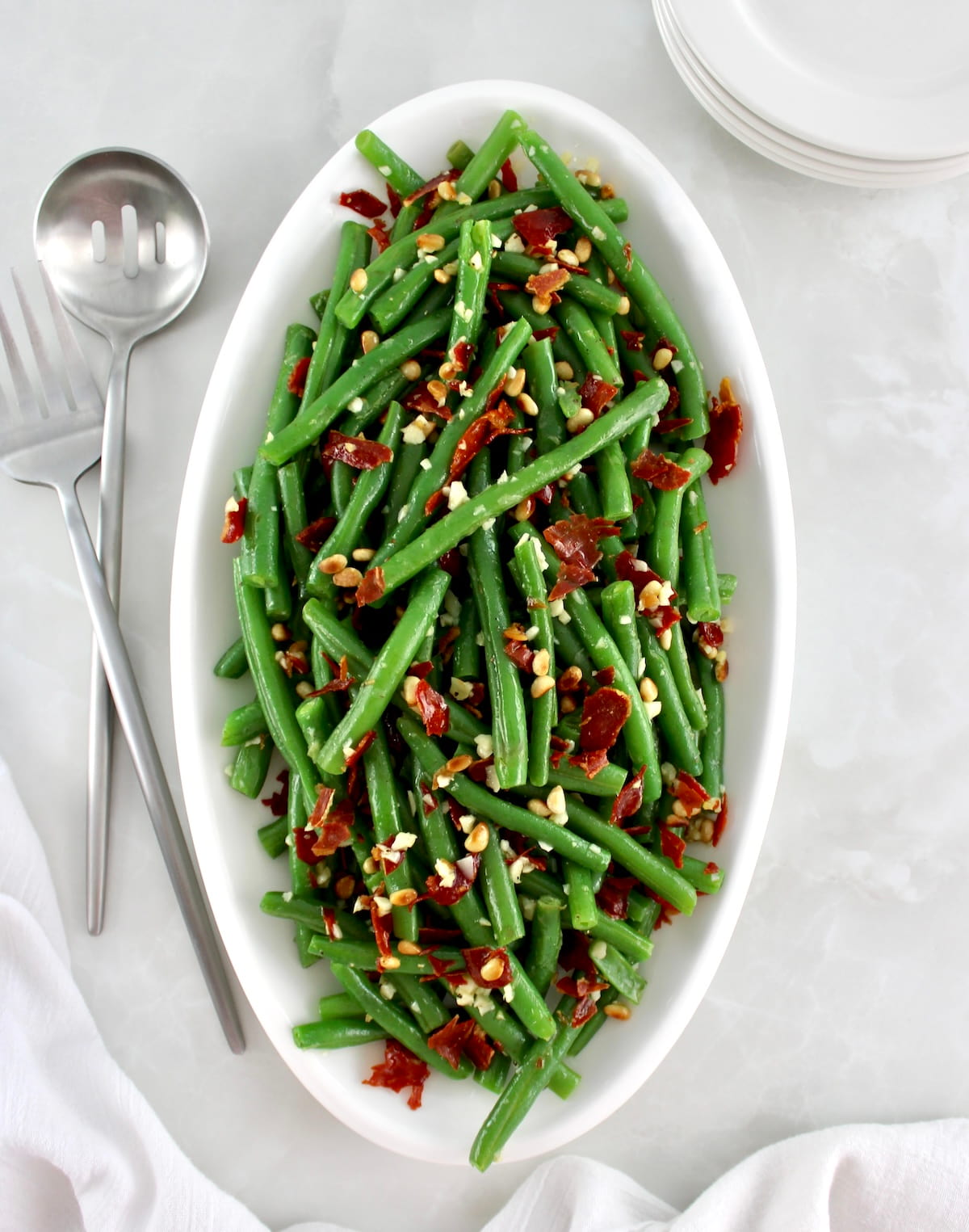 overhead view of Green Beans with Crispy Prosciutto on white oval platter with serving utensils on side