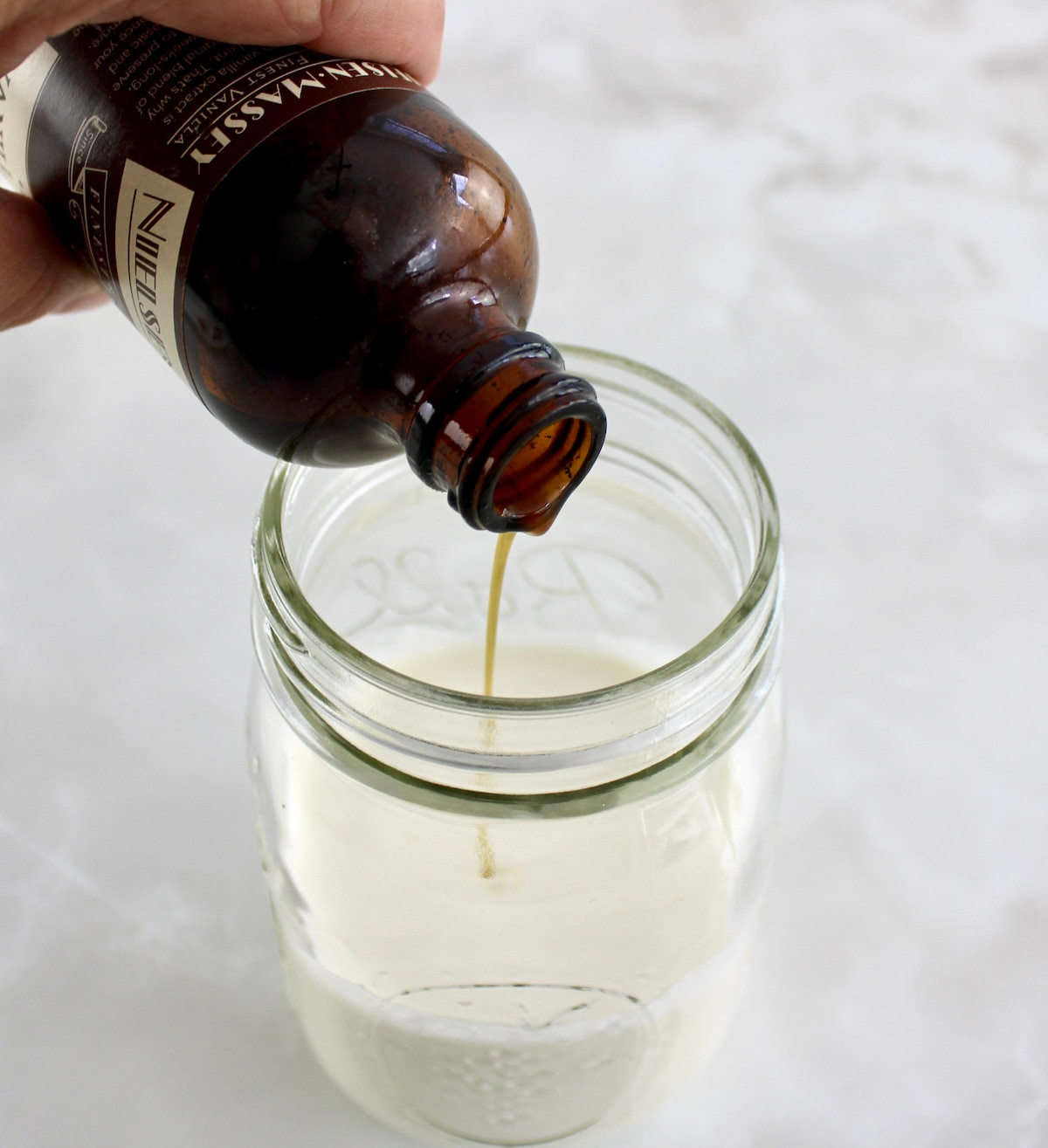 vanilla extract being poured into glass jar with heavy cream