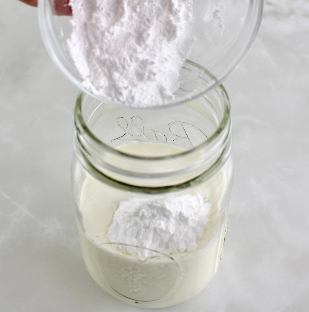 powdered allulose being poured into mason jar with heavy cream