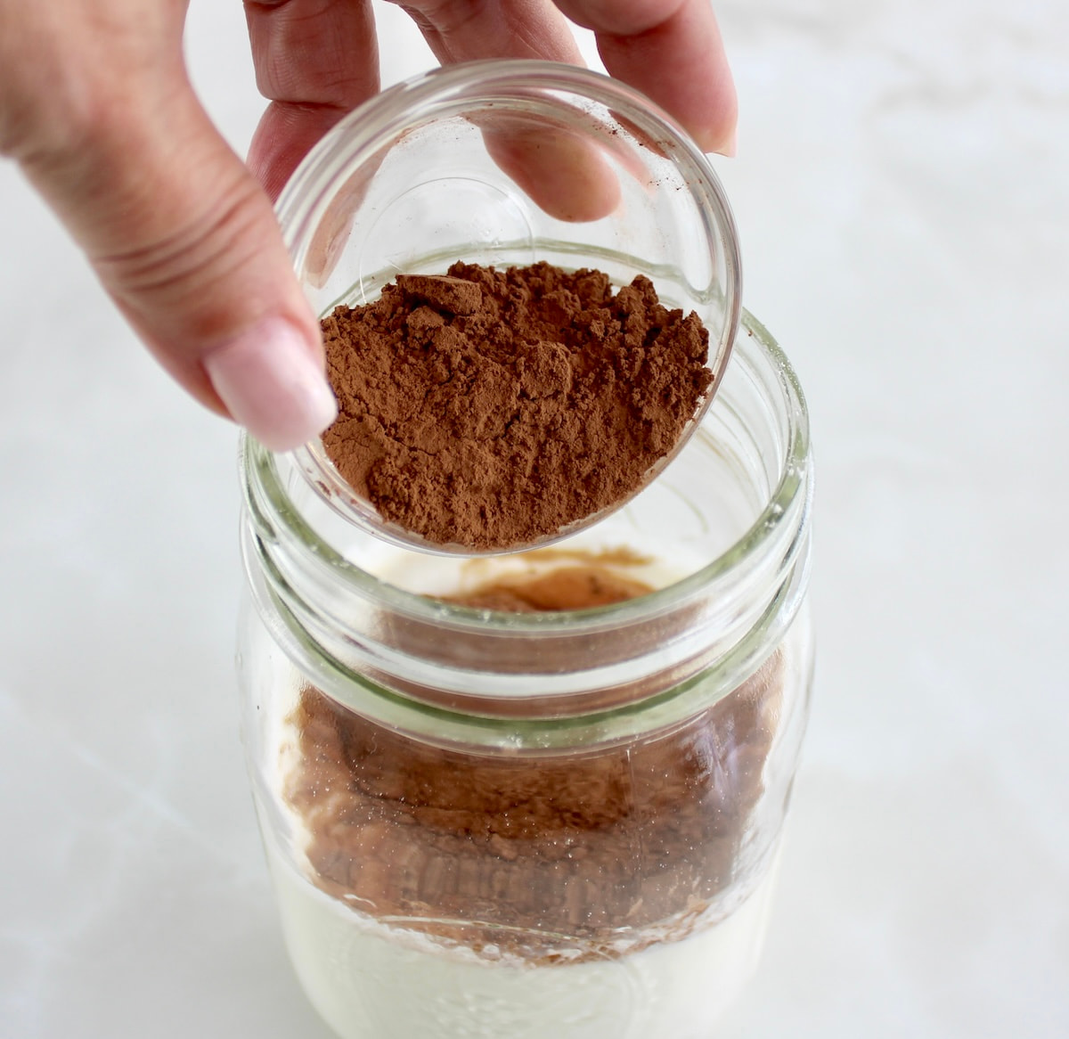 cocoa powder being poured into mason jar with heavy cream