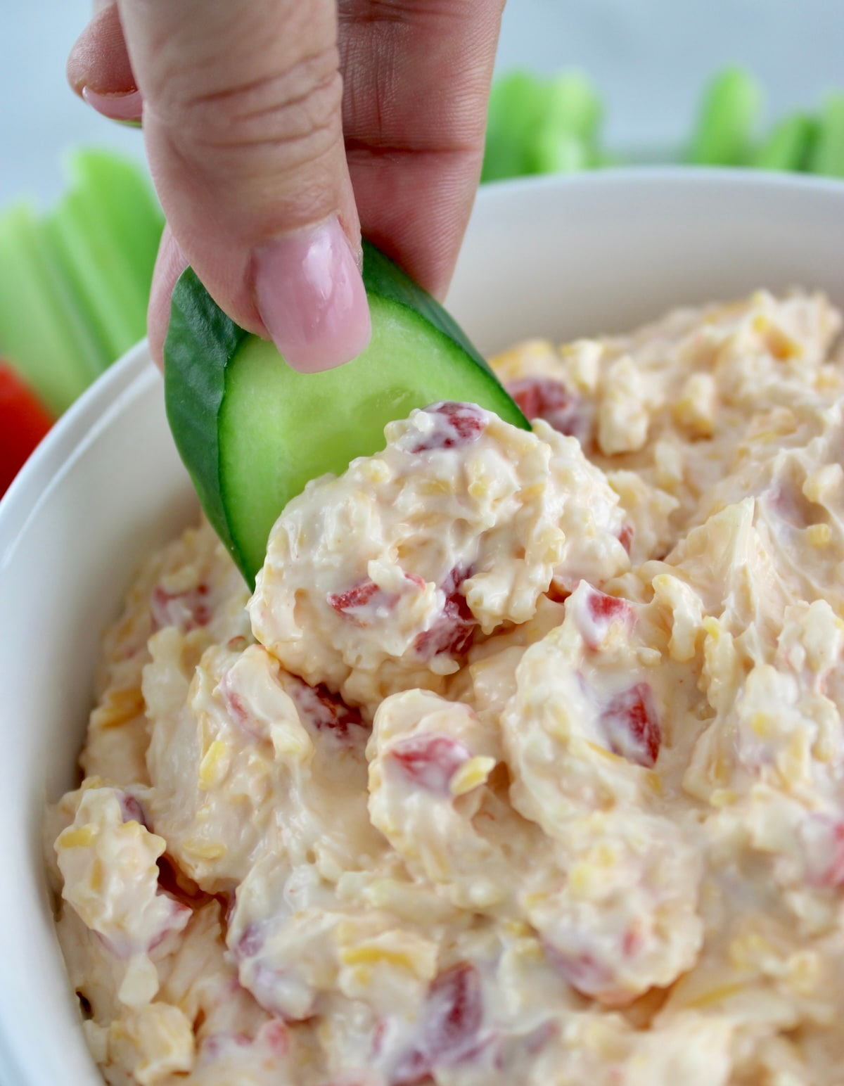 Pimento Cheese Spread in white bowl with cucumber slice dipping in