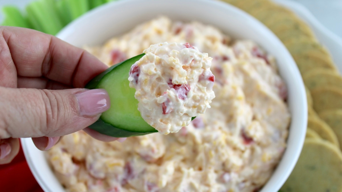 closeup of Pimento Cheese Spread on end of slice of cucumber with dip in white bowl in back
