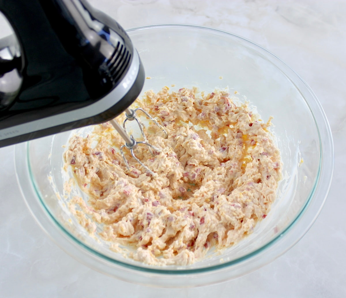 Pimento Cheese Spread being mixed in glass bowl with hand mixer 