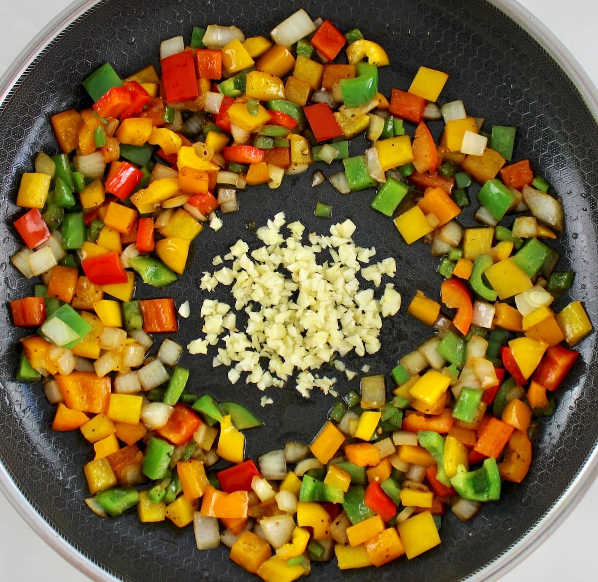 chopped red, yellow, orange and green bell peppers and onions in skillet with minced garlic in center