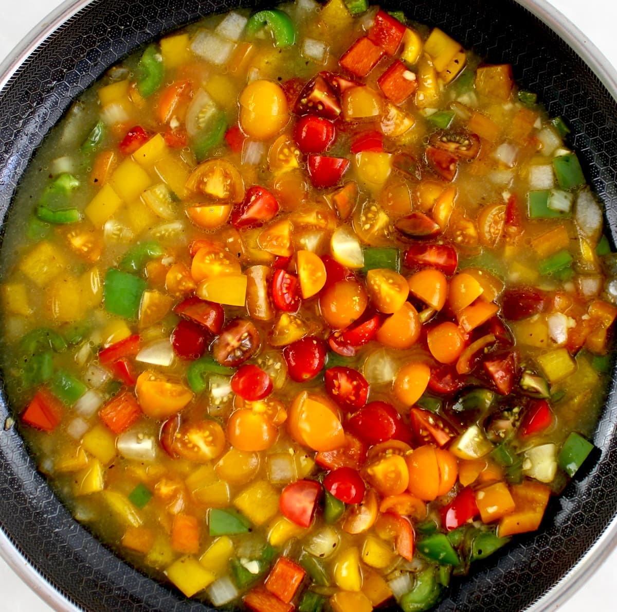 chopped tomatoes, red, yellow, orange and green bell peppers and onions in skillet with broth