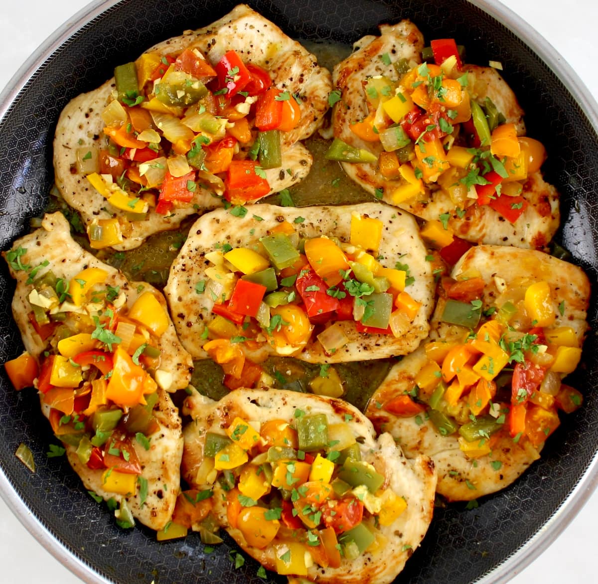 chopped peppers and tomatoes over chicken breasts in skillet
