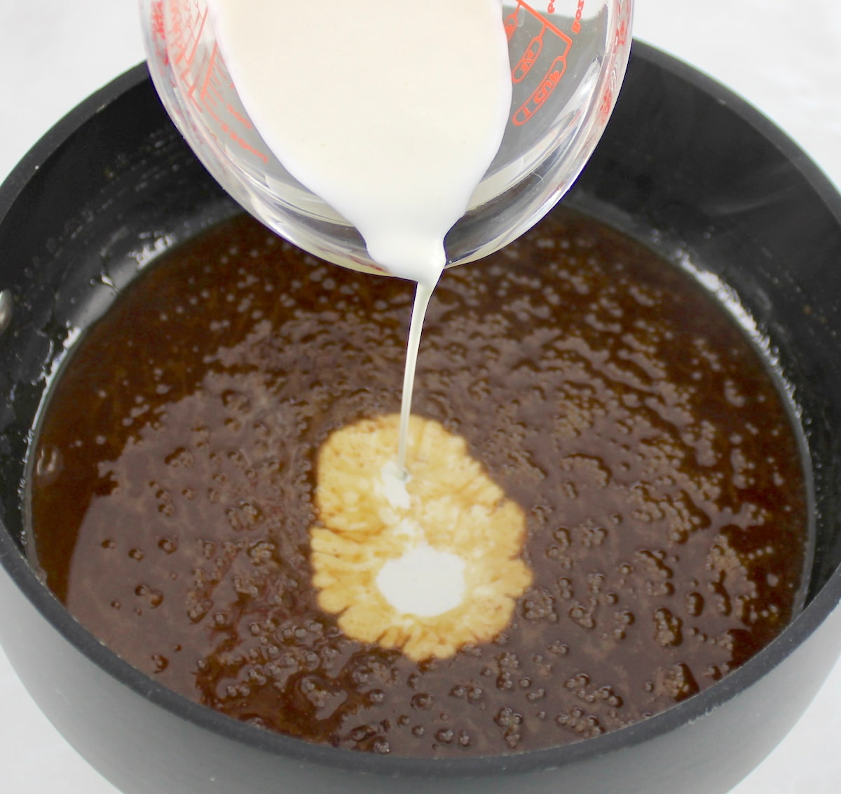 heavy cream being poured into caramel mix in saucepan