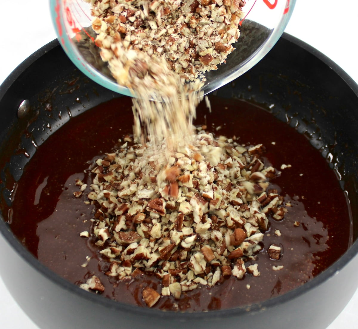pouring chopped pecans into caramel in saucepan