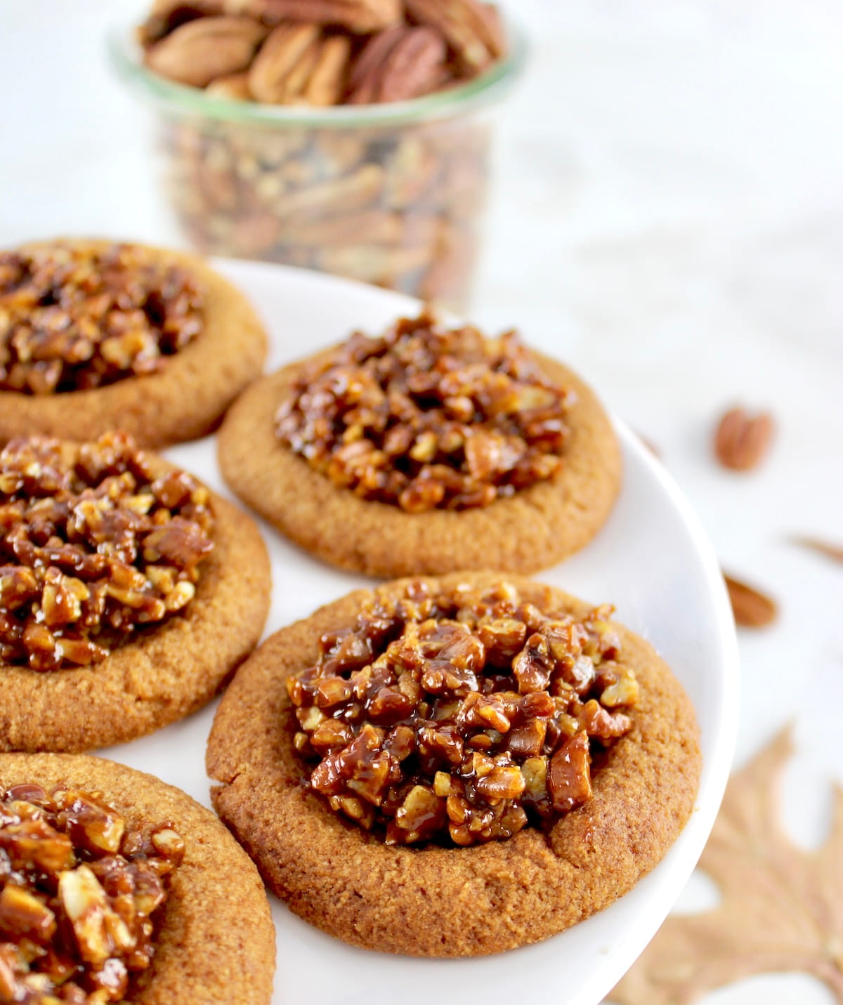 closeup of Pecan Pie Cookies on cooling rack with pecans in open glass jar in back