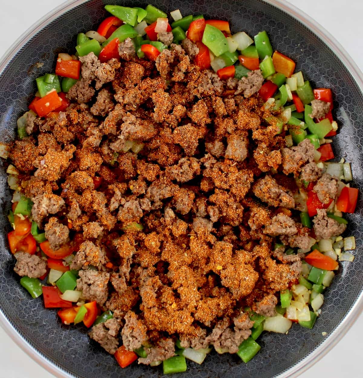taco meat in skillet over sauteed peppers and onions