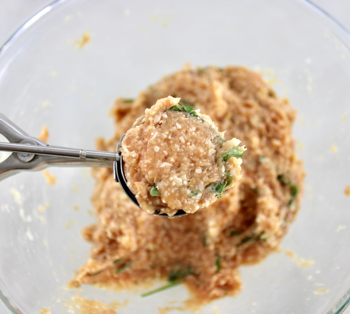 Chicken Parmesan Meatballs mix in cookie scoop held up over glass bowl