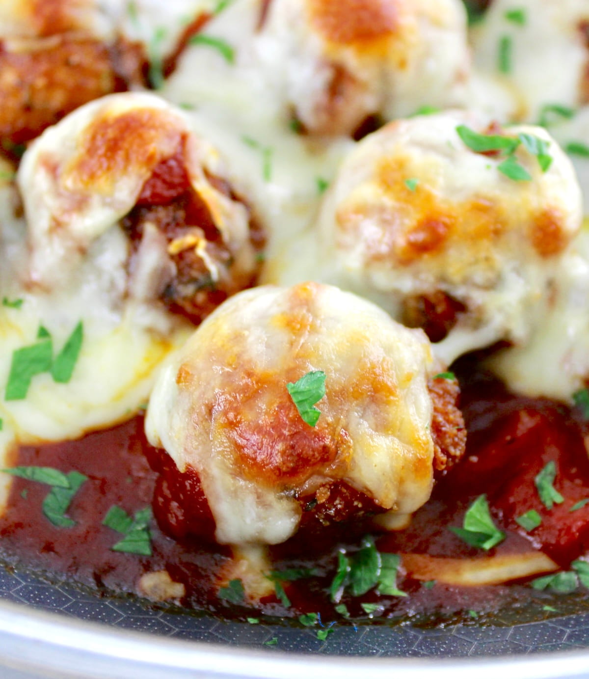 closeup of Chicken Parmesan Meatballs in skillet with melted cheese on top