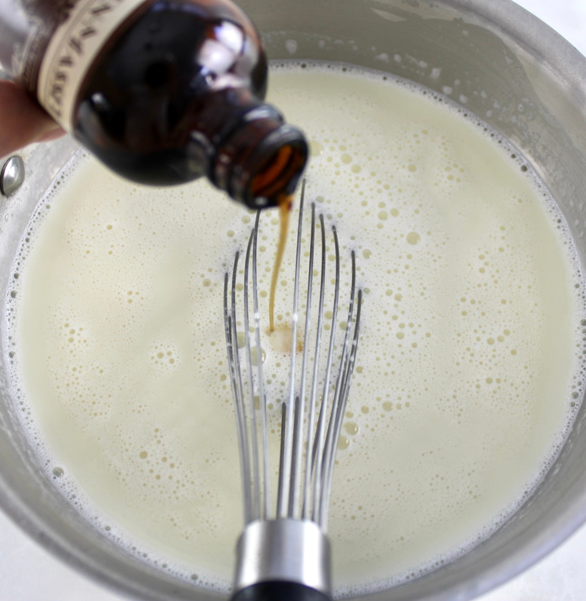 vanilla extract being poured into Peppermint White Hot Chocolate in pot
