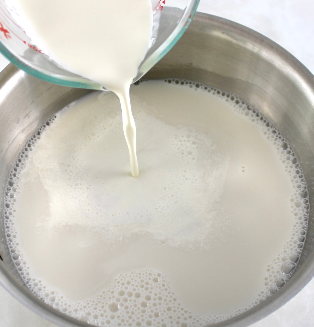 heavy cream being poured into pot with almond milk