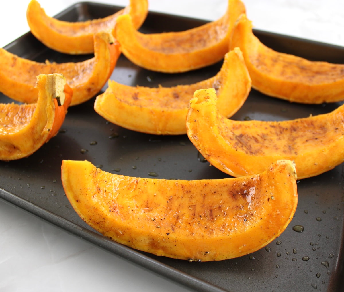 8 pumpkin wedges on baking sheet with pumpkin spice, salt and pepper