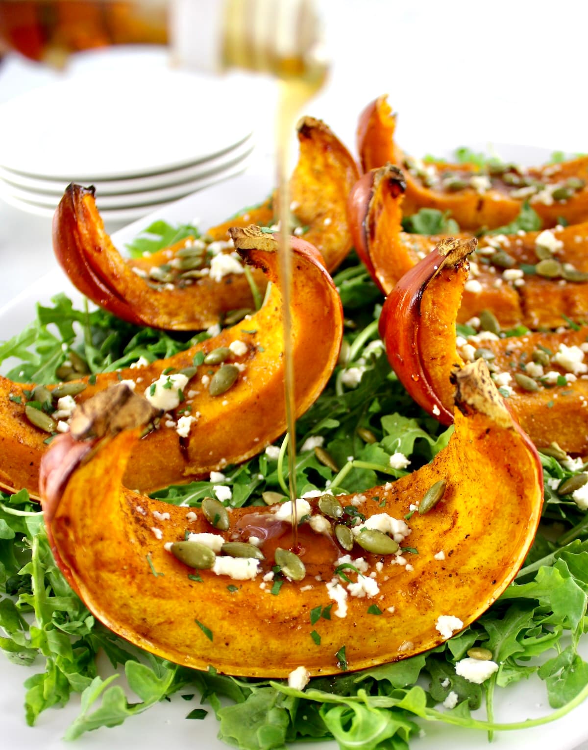 closeup of Roasted Pumpkin on bed of arugula with maple syrup pouring on top