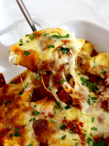 spoon lifting a Stuffed Shells with Meat Sauce out of casserole with cheese pulling