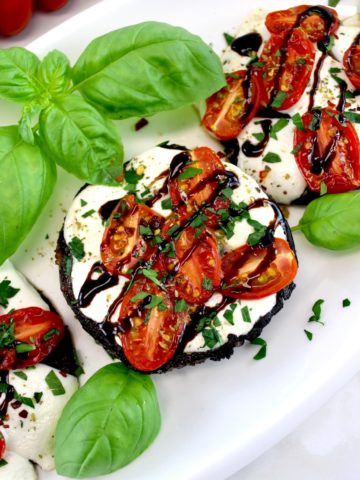 closeup of Caprese Stuffed Portobellos on white plate with balsamic drizzle and fresh basil