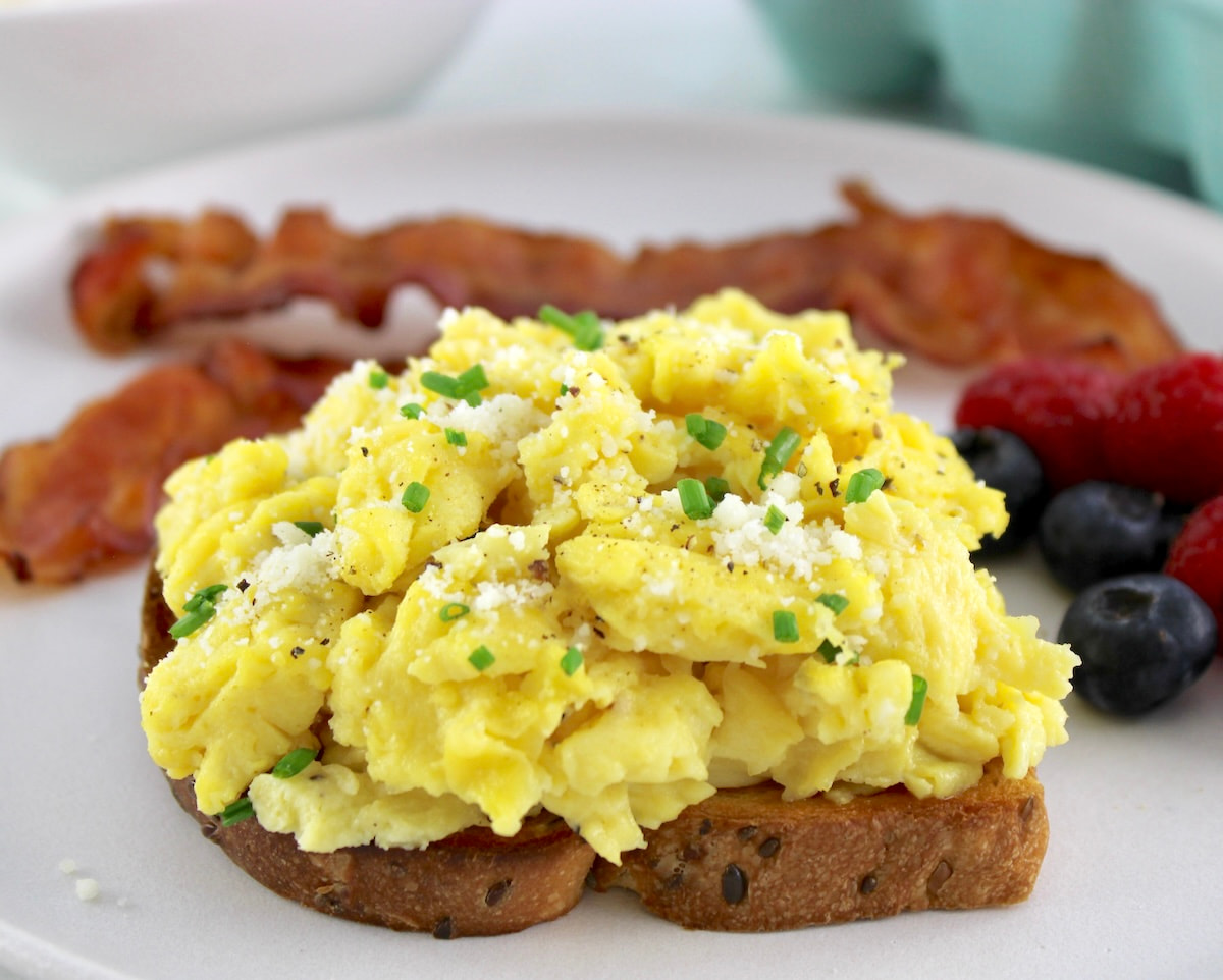 Ricotta Scrambled Eggs on piece of taste with berries and bacon in back