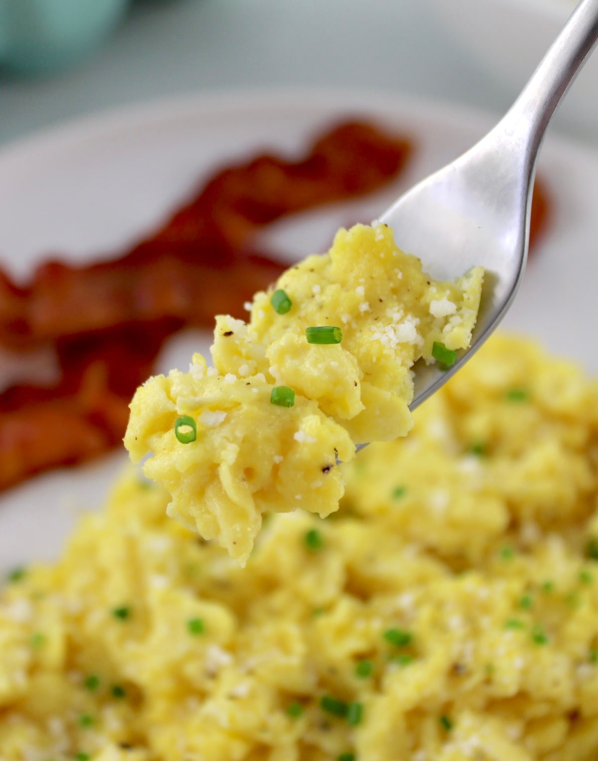 Ricotta Scrambled Eggs on white plate with bacon and fork holding up some