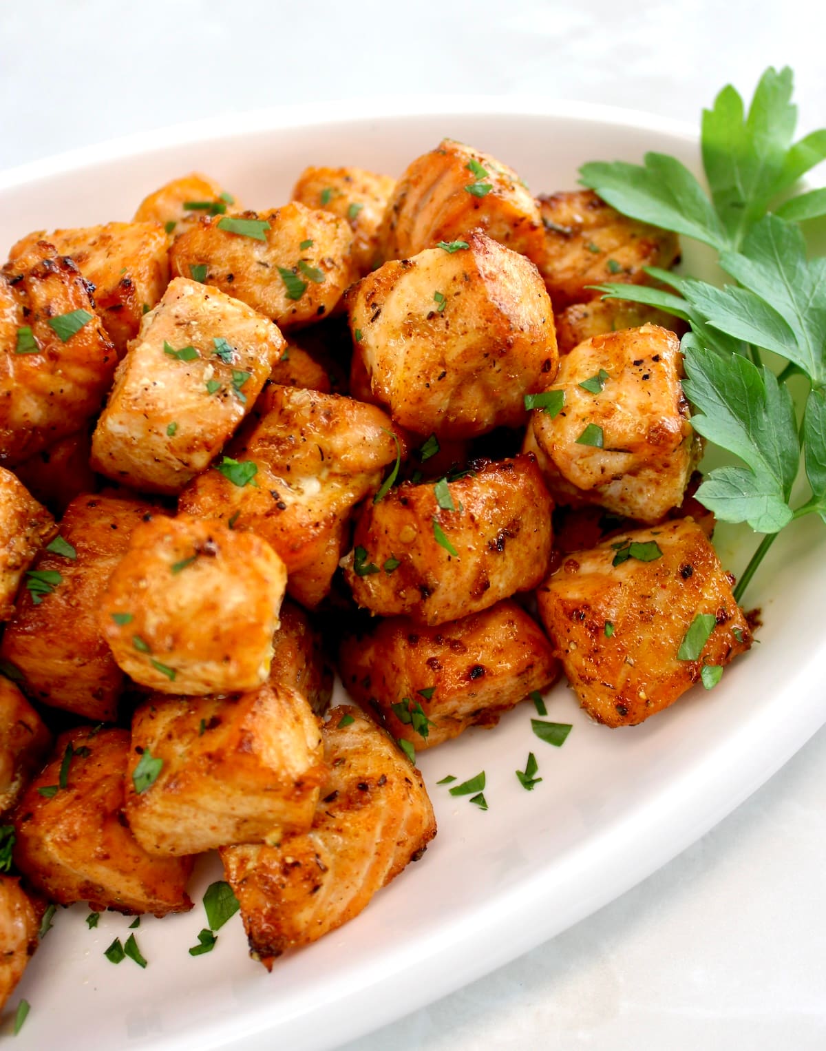 closeup of Cajun Salmon Bites on white oval platter with parsley garnish