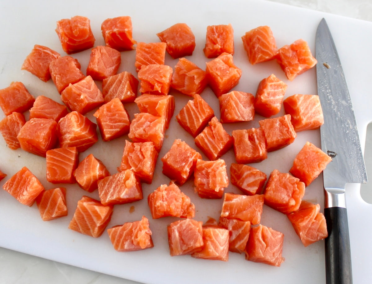 fresh salmon on white cutting board with knife cut into chunks