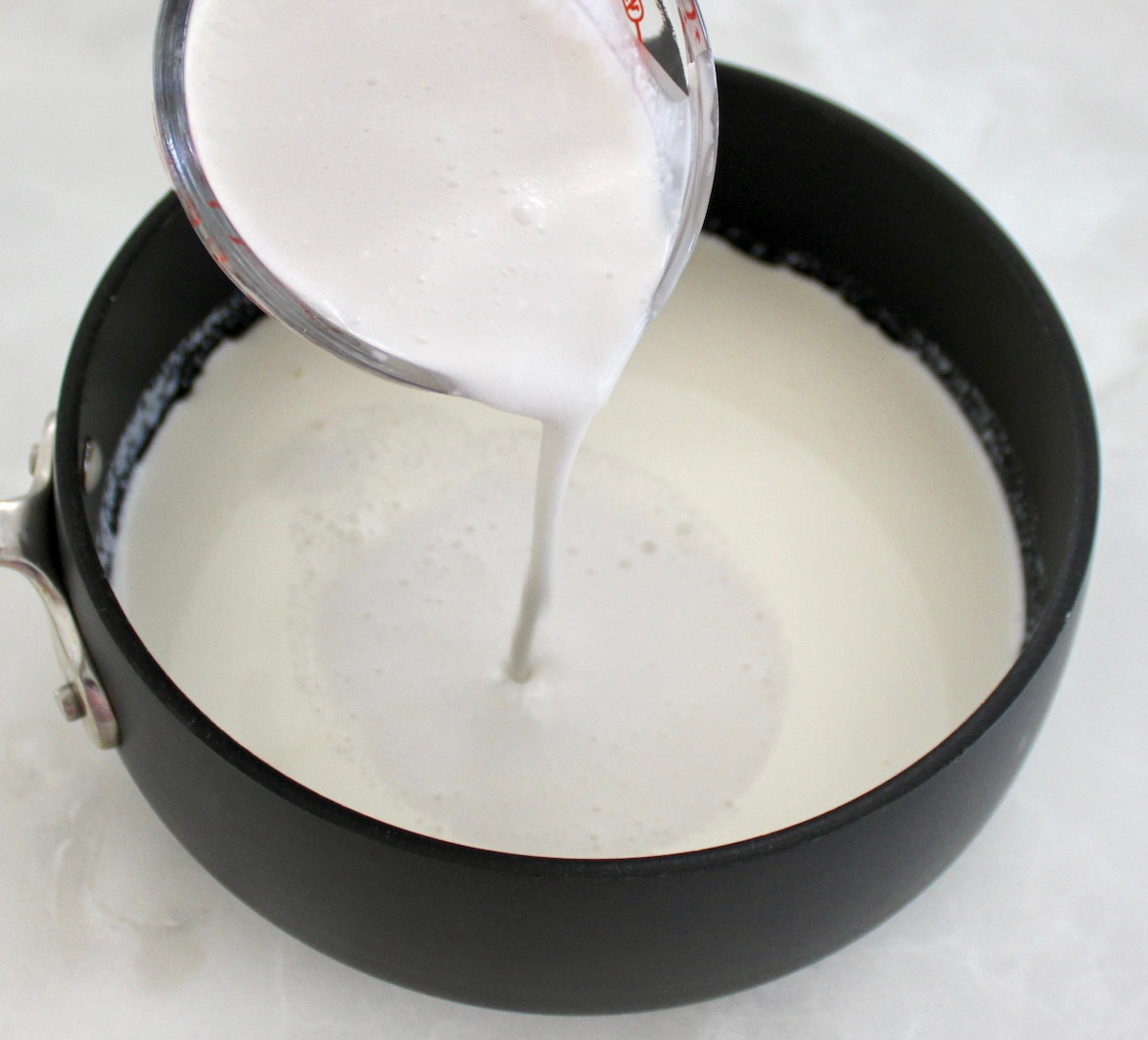 coconut milk being poured into a saucepan with heavy cream