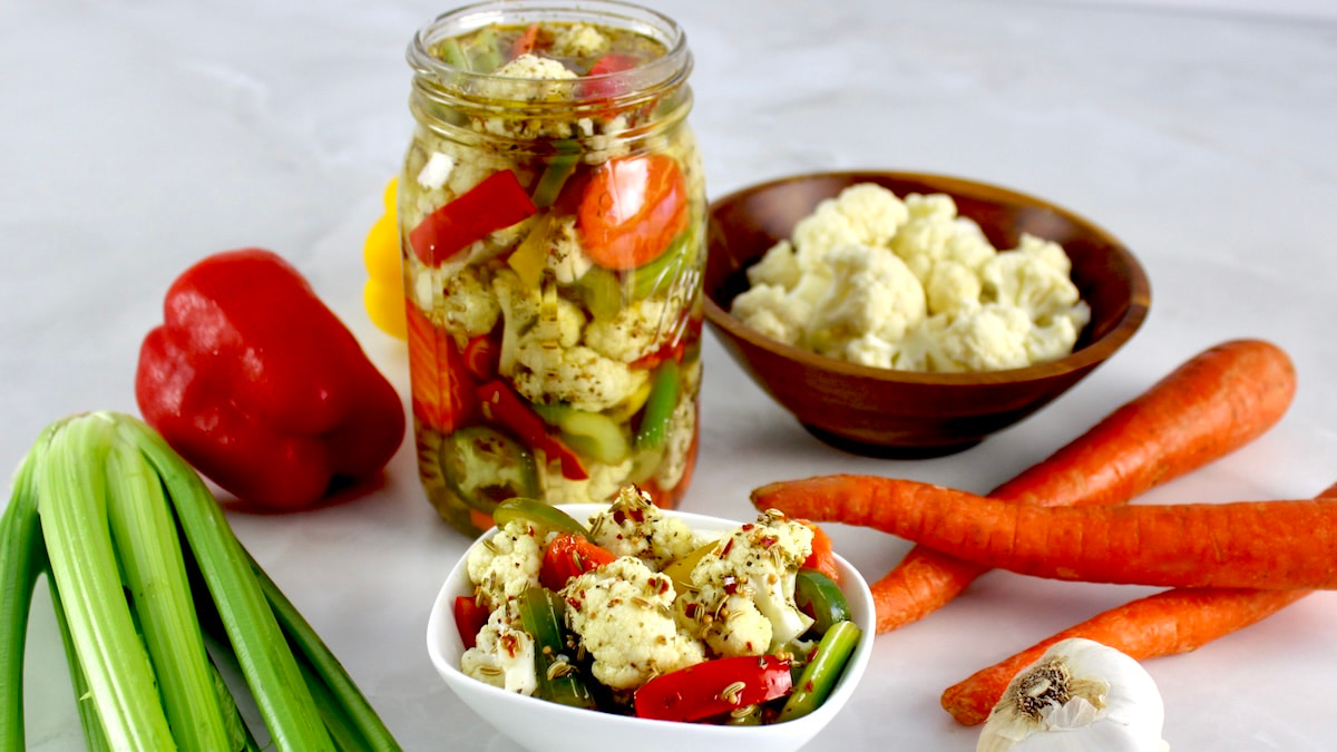 Easy Homemade Giardiniera in white bowl with more in glass jars and veggies in back