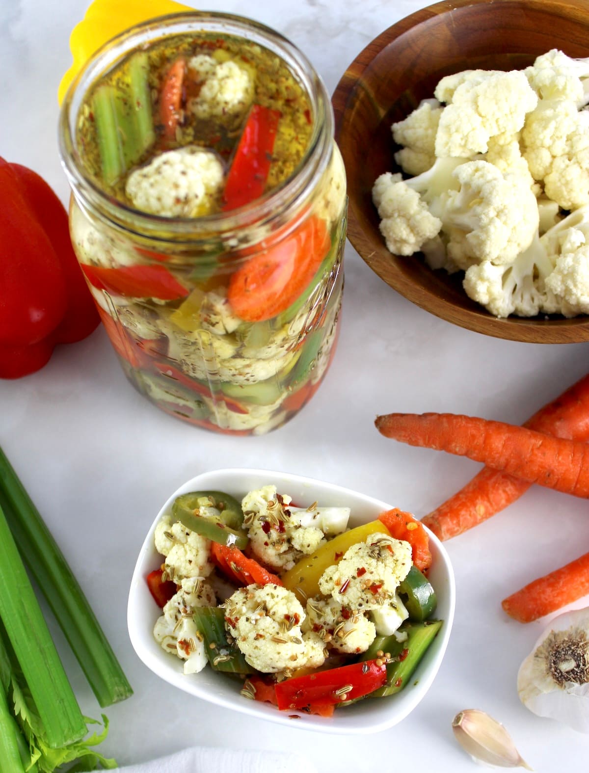 overhead view of Easy Homemade Giardiniera in white bowl and glass jar with veggies all around