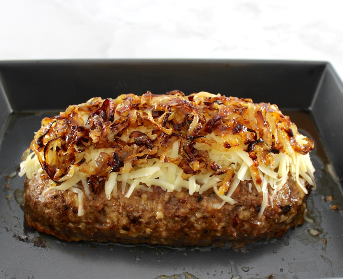 French Onion Meatloaf in baking pan with shredded gruyere and caramlized onions on top