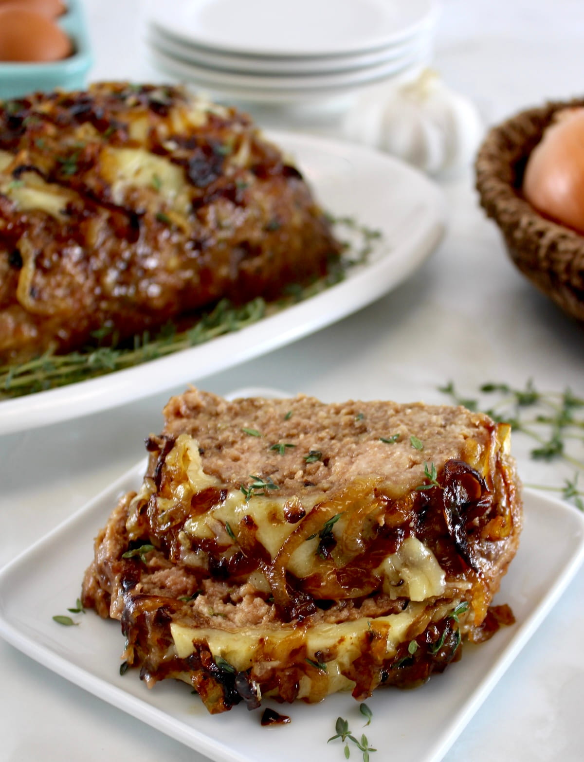 2 slices of French Onion Meatloaf stacked up on white plate with more meatloaf in back