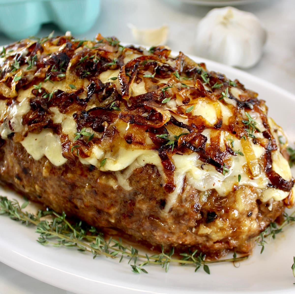 closeup of French Onion Meatloaf on white platter with fresh thyme